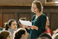 A female professor teaches at the front of a classroom.